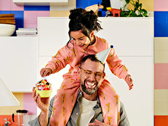Two people with party hats in kitchen, one holding ice cream.