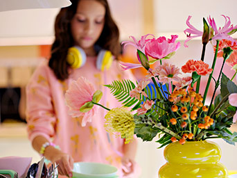 Flower bouquet in yellow vase, person in background with headphones.