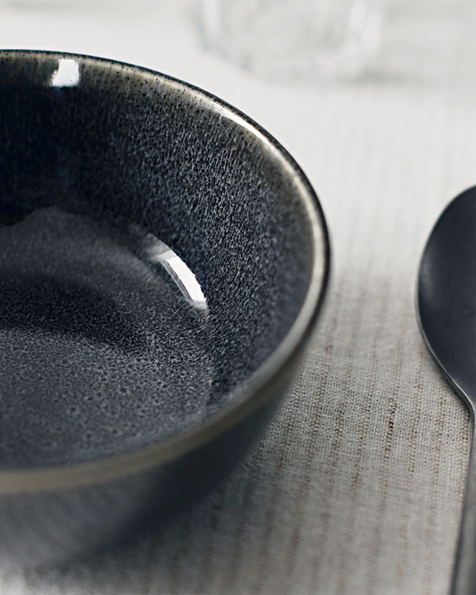Empty dark ceramic bowl on light fabric with spoon.
