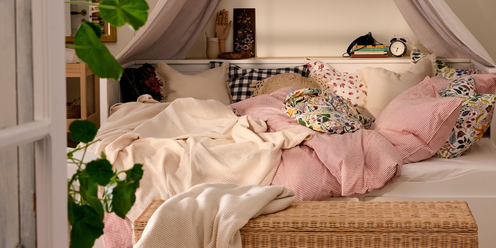 HEMNES day-bed with bedlinen in pink and white, TOLKNING rattan bench in foreground, a mirror and a textile canopy above bed.
