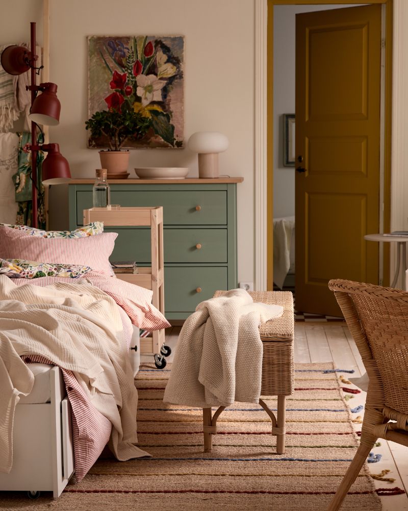 A one-bedroom apartment with HEMNES day-bed, a rattan chair in the foreground and a green HEMNES chest of drawers in the back.