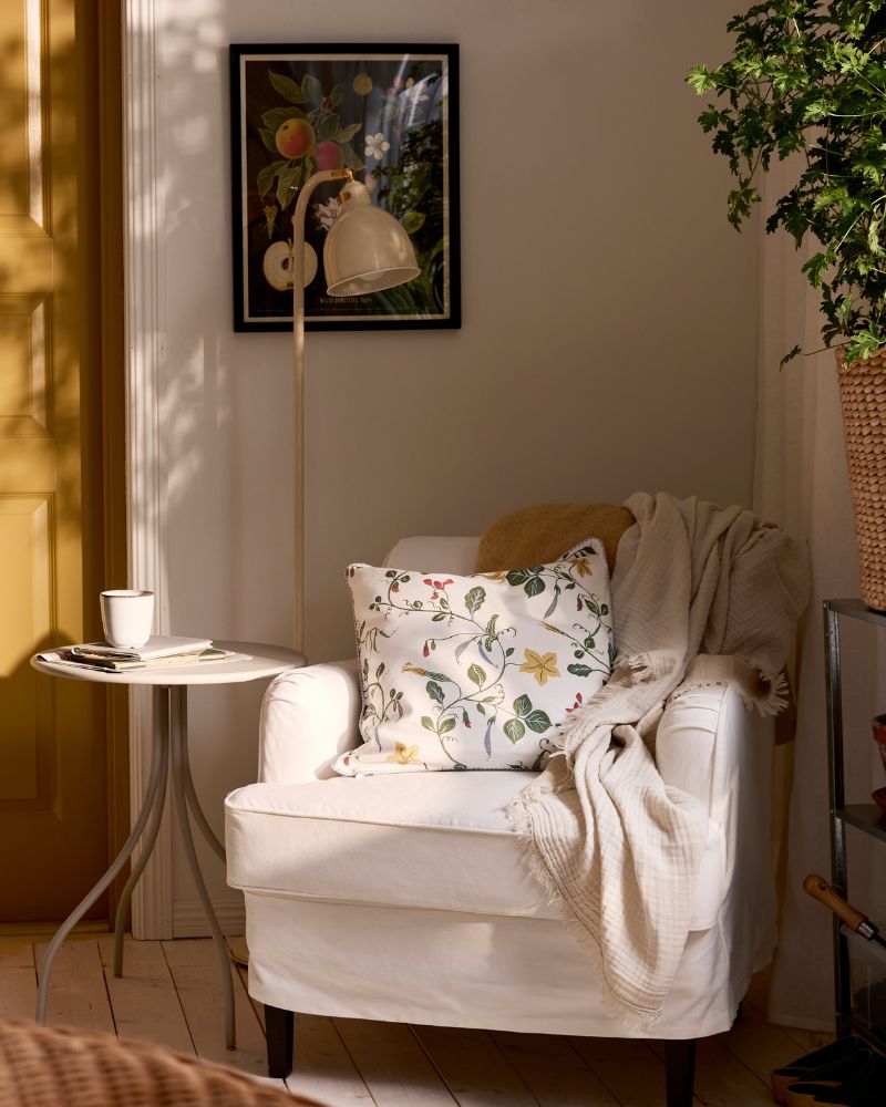 Corner of a room with a white ROCKSJÖN armchair with a side table and reading lamp, and green plant on the other side.