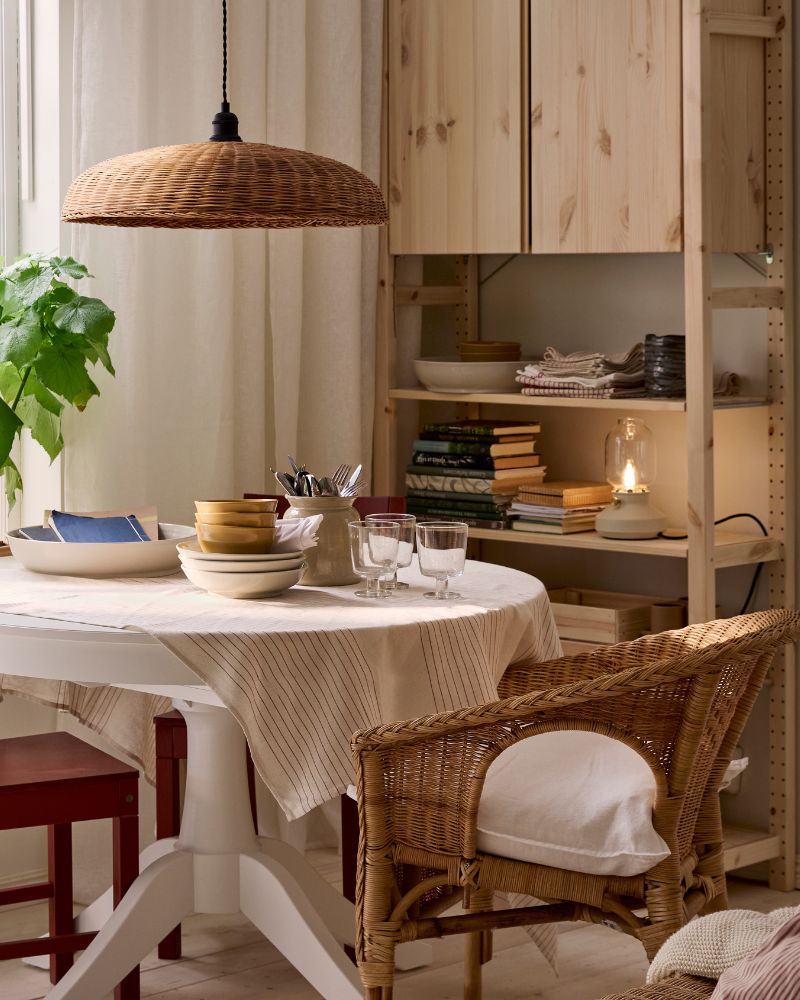 A white ROSENTORP table by a window, IVAR shelving unit behind it and diferent kinds of chairs. Plants on the windowsill.
