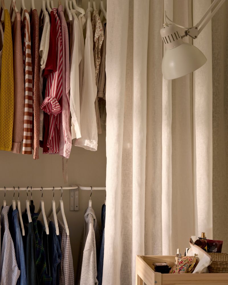 A storage solution with clothes hanging on rods at two dierent heights, with a white curtain half open in front of it.