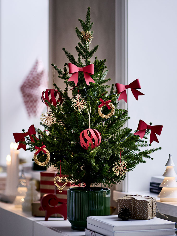 Un pequeño árbol de Navidad en maceta se decora con adornos rojos y dorados VINTERFINT y se coloca sobre un aparador.