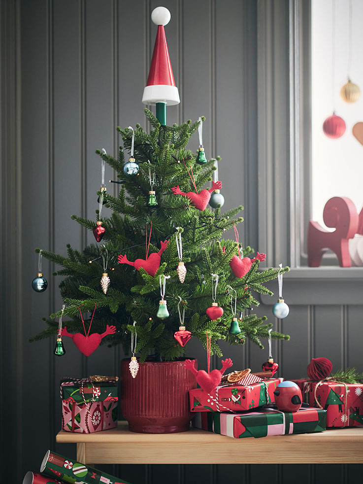 Un pequeño árbol de Navidad en maceta está decorado con divertidos adornos VINTERFINT y colocado sobre un banco con regalos encima.
