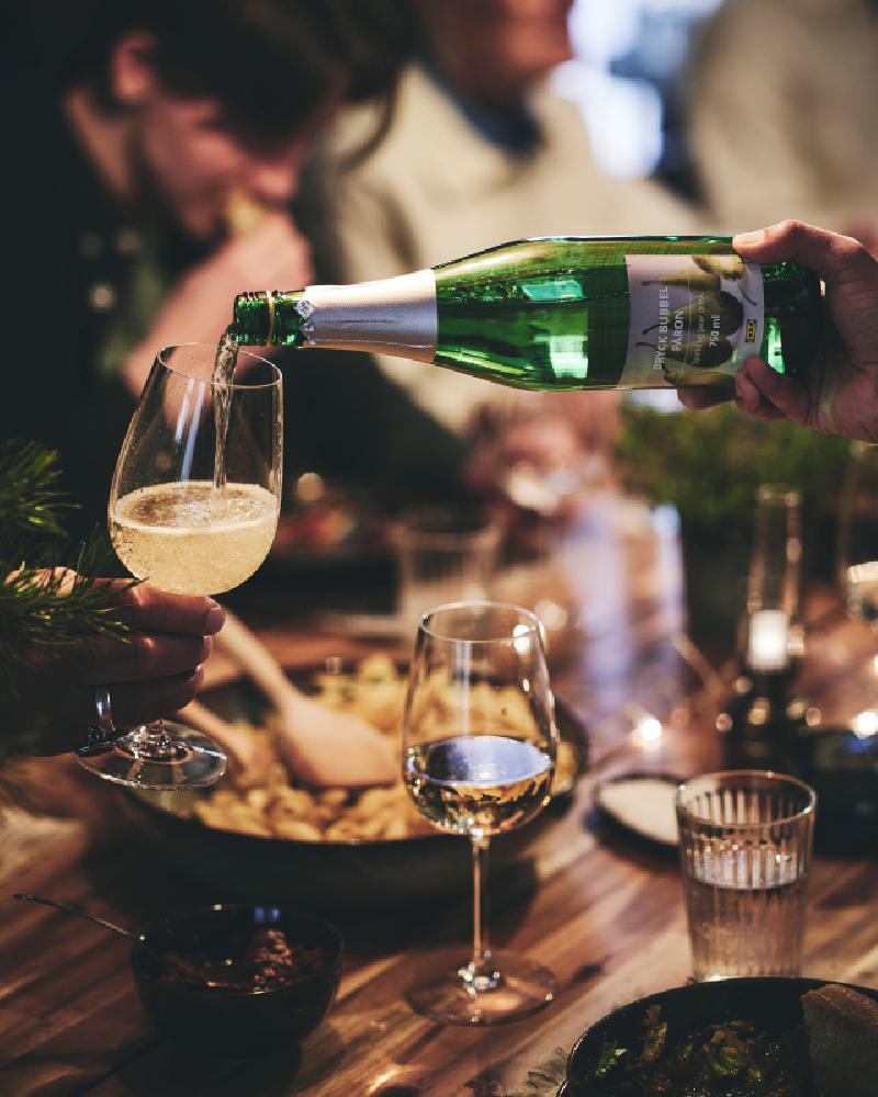 Un invitado a una cena sirve una copa de bebida espumosa en la copa de vino de otro invitado.