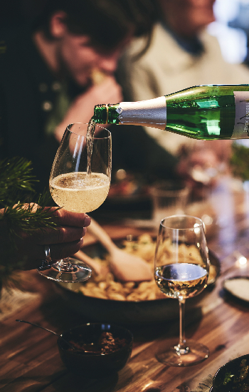 Un invitado a una cena sirve una copa de bebida espumosa en la copa de vino de otro invitado.