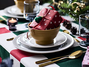 Un pequeño regalo reposa en un cuenco sobre una mesa festiva, envuelto en papel de regalo rojo VINTERFINT con un estampado de copos de nieve.