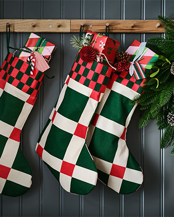 Tres calcetines navideños VINTERFINT con un llamativo estampado a cuadros verdes y rojos cuelgan de percheros con pomos.