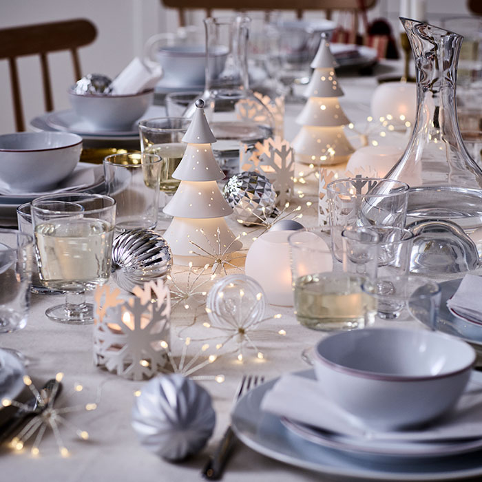 Las decoraciones VINTERFINT y la iluminación STRÅLA adornan una mesa decorada de forma festiva en tonos blancos y plateados.