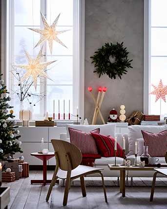 Una acogedora sala de estar con ventanas altas decorada para Navidad con adornos VINTERFINT e iluminación STRÅLA.