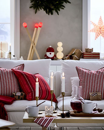 Tres fundas de cojín VINTERFINT con rayas rojas están sobre un sofá, en una sala de estar decorada para Navidad.