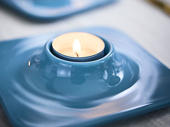 Unos portavelas VINTERFINT de color azul claro tienen velas encendidas en su interior, ambos están sobre una mesa.