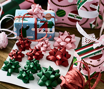 Un conjunto de lazos de regalo VINTERFINT en verde, rojo y rosa rodeado de cintas, paquetes envueltos y envoltorios de regalo.