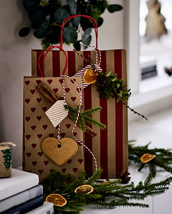 Dos bolsas de regalo VINTERFINT, una con un estampado de corazones y otra con rayas, se encuentran en una caja de madera junto a un pequeño jarrón.