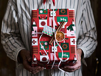 Una persona con una camiseta a rayas sostiene un regalo envuelto en papel de regalo VINTERFINT y adornado con un fruto seco.