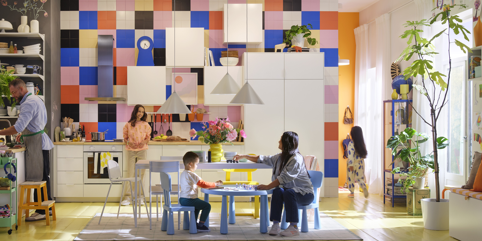 Cocina colorida y luminosa de estilo familiar, con personas cocinando, jugando y compartiendo en un ambiente acogedor y funcional.