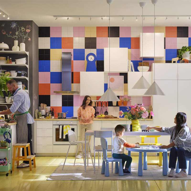 Cocina colorida y luminosa de estilo familiar, con personas cocinando, jugando y compartiendo en un ambiente acogedor y funcional.