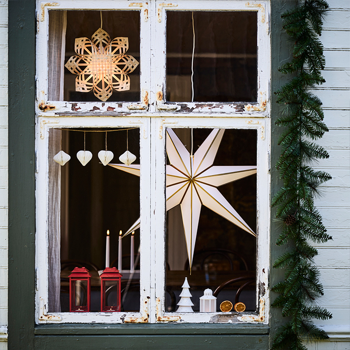 Ventana de madera blanca desgastada con varias estrellas de papel de diferentes formas colgadas en el interior.