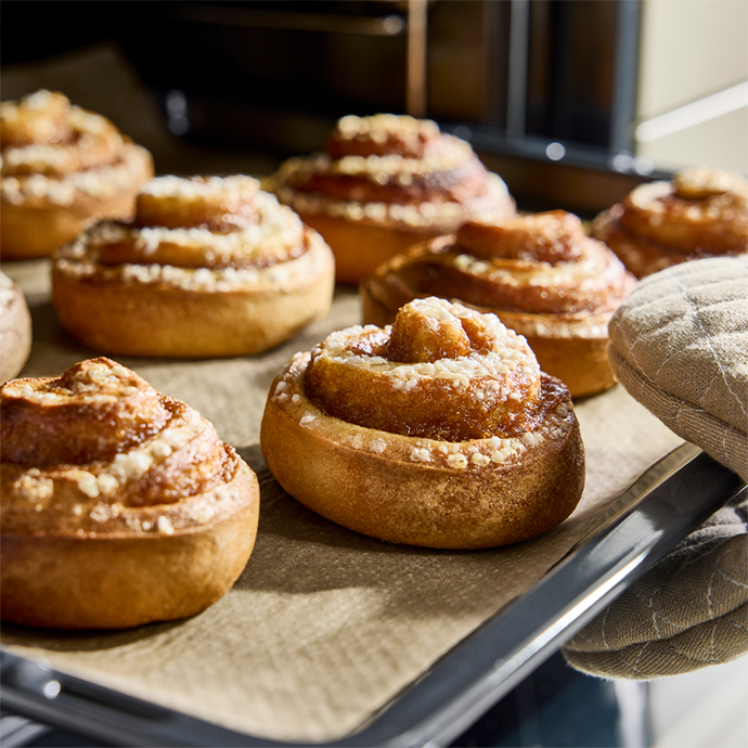 Freshly baked cinnamon buns on baking paper on a tray. Several buns are visible, ready to be served.