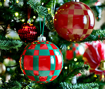 Primer plano de adornos navideños de gran tamaño, con diseño de cuadros rojos y verdes, colgando de un árbol de Navidad iluminado.	