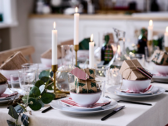 Christmas table decorated with candles and white tableware, with gifts for each guest on their plates.