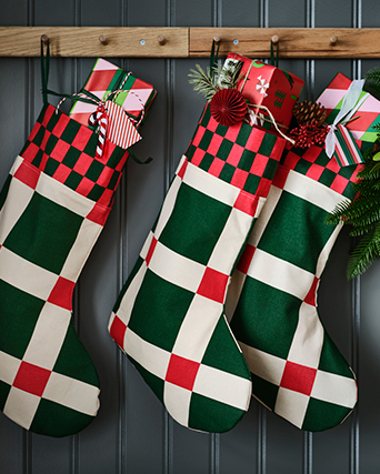 Three Christmas stockings, in green and red colours, hanging from a coat rack and filled with presents.
