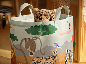 Cesto de almacenaje redondo de tela con asas y estampado de safari, con la cabeza de un leopardo de peluche asomando por el borde.