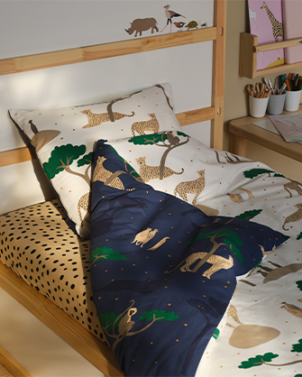 Cama infantil con marco de madera clara y ropa de cama de algodón con estampado de leopardos y árboles, en colores blanco, beige y azul oscuro.