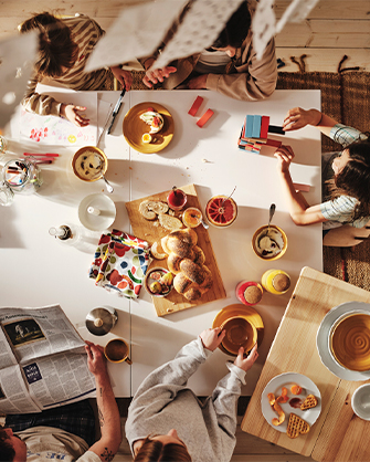 Vista superior de una mesa de comedor extensible blanca durante un desayuno familiar, con cuencos de cerámica amarilla, pan trenzado y utensilios de arte.