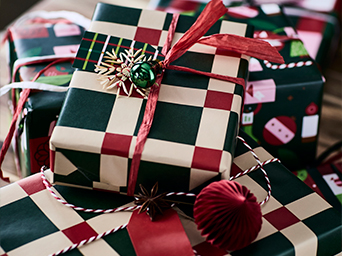 Close-up of Christmas gifts wrapped in red, green, and beige checker-patterned paper, tied with ribbons and hanging snowflake ornaments.