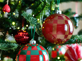 Detail of the tree with large glass or plastic Christmas baubles in red and green, with checkered and candy cane designs, among the branches and LED lights.