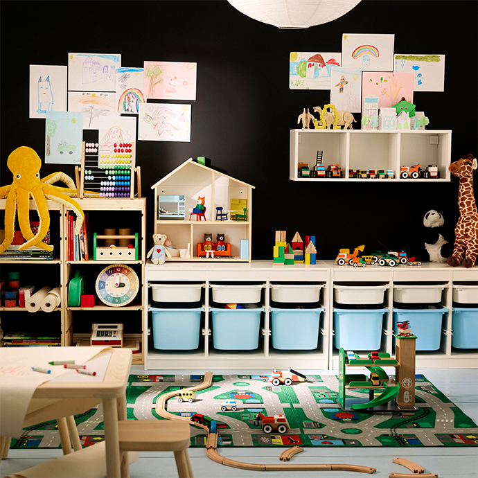 Playroom with black wall, a white cube storage system with blue plastic drawers, a printed road rug, and a wooden art table.