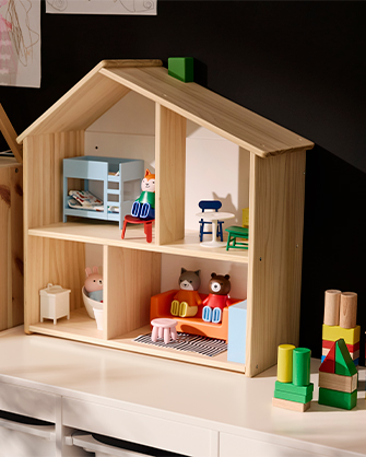 Close-up of a two-story untreated pine wood dollhouse with a pitched roof and brightly colored miniature furniture.