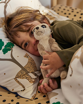 A child is cuddling with a soft toy meerkat in a bed with a white/dark blue SANDLÖPARE duvet cover and pillowcase.