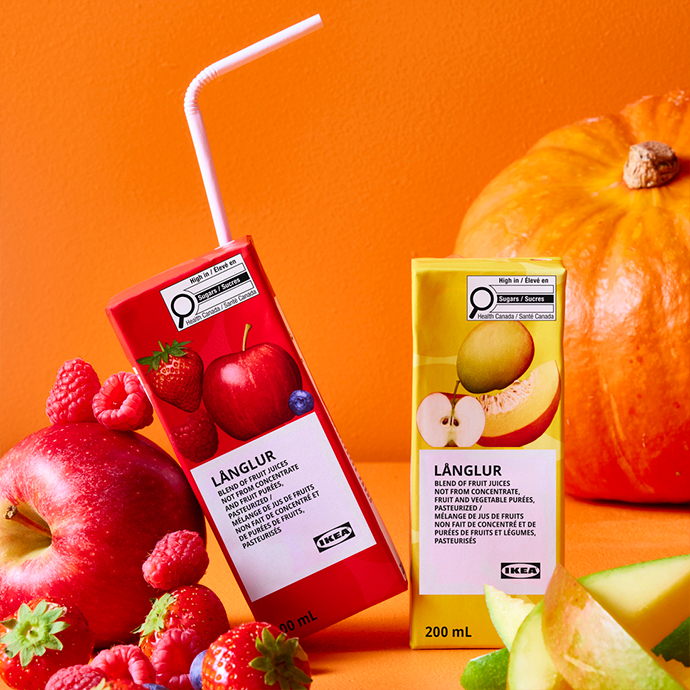Envases de zumo LÄNGLUR en sabores frutos rojos y manzana con frutas frescas y calabaza sobre fondo naranja
