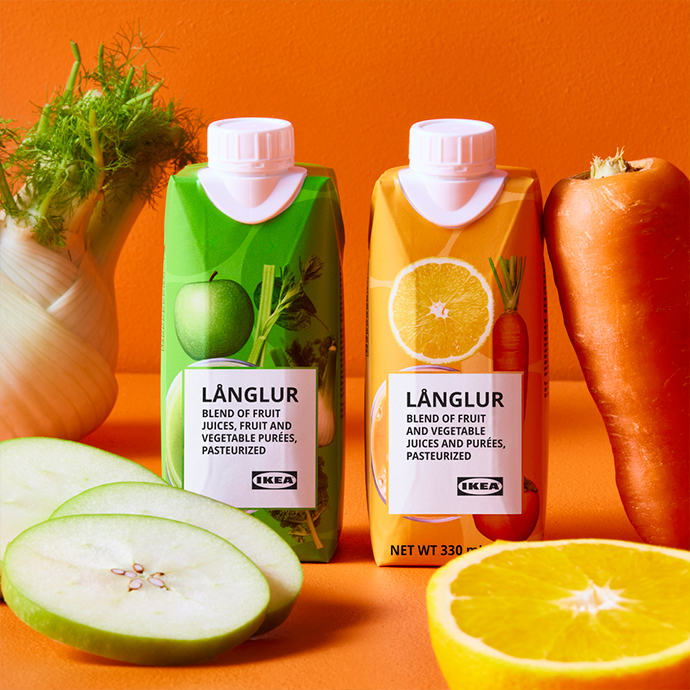 Dos envases de zumo LÄNGLUR en packaging verde y naranja junto a zanahorias frescas y manzana cortada sobre fondo naranja