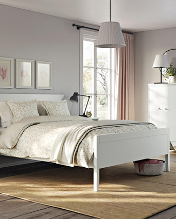 Bright and calm bedroom with a white bed, cream floral bedding, black nightstand, and wardrobe.