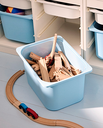 Organized toy storage: Low cabinet with drawers and blue bins filled with wooden blocks, toy trains, and wooden vehicles. Practical solutions for the children's room.
