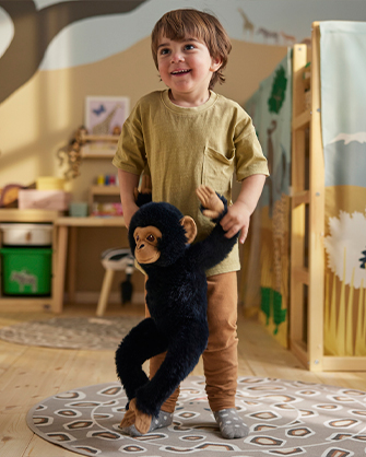 Smiling child playing in his safari-themed children's room, hugging a black monkey stuffed toy. Encourages role-play and imagination in a safe environment.