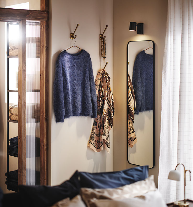 Rincón de un dormitorio con espejo LINDBYN y ganchos para ropa y accesorios en las paredes. Puertas y ventana de cristal a los lados.