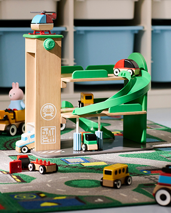 Wooden parking garage toy with spiral ramp and car elevator. Small toy cars parked on play mat with road markings