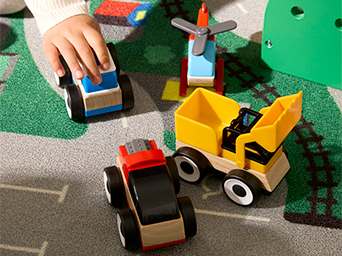 Child playing with colorful toy trucks and construction vehicles on a play mat with roads and green spaces