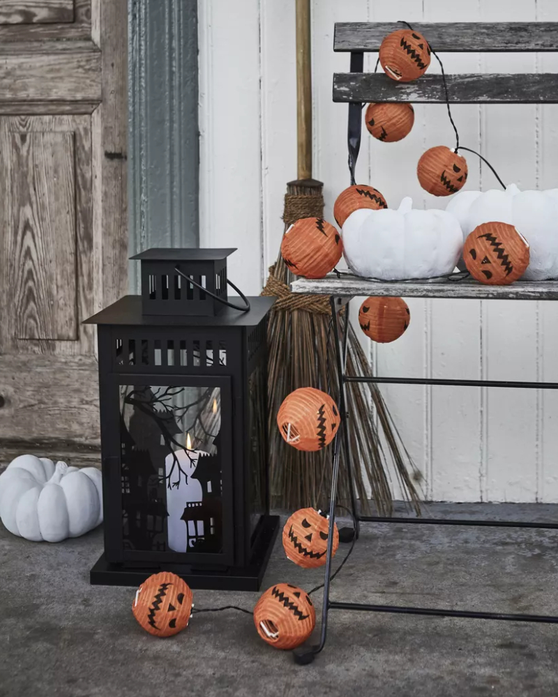A KUSTFYR light chain featuring several small ghosts is wrapped around a black decoration and placed on top of some books.