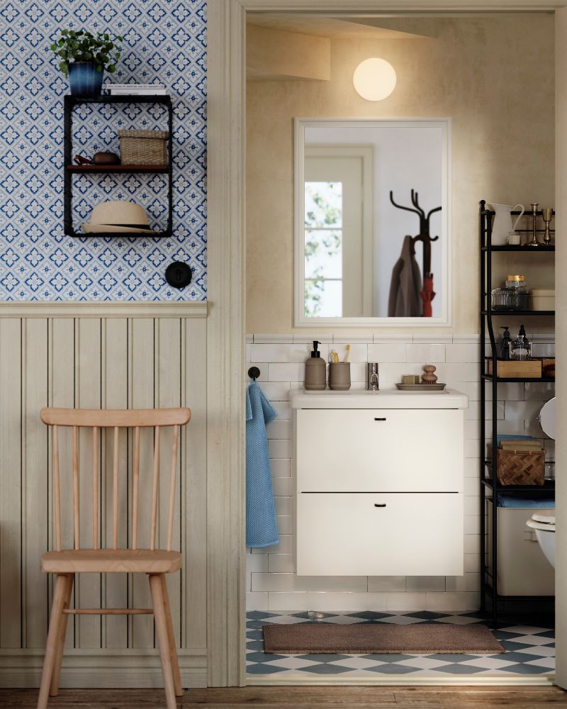 Un lavabo con cajones ENHET/TVÄLLEN en color blanco se apoya sobre una pared con azulejos tipo metro, en un aseo de estilo tradicional situado bajo una escalera.