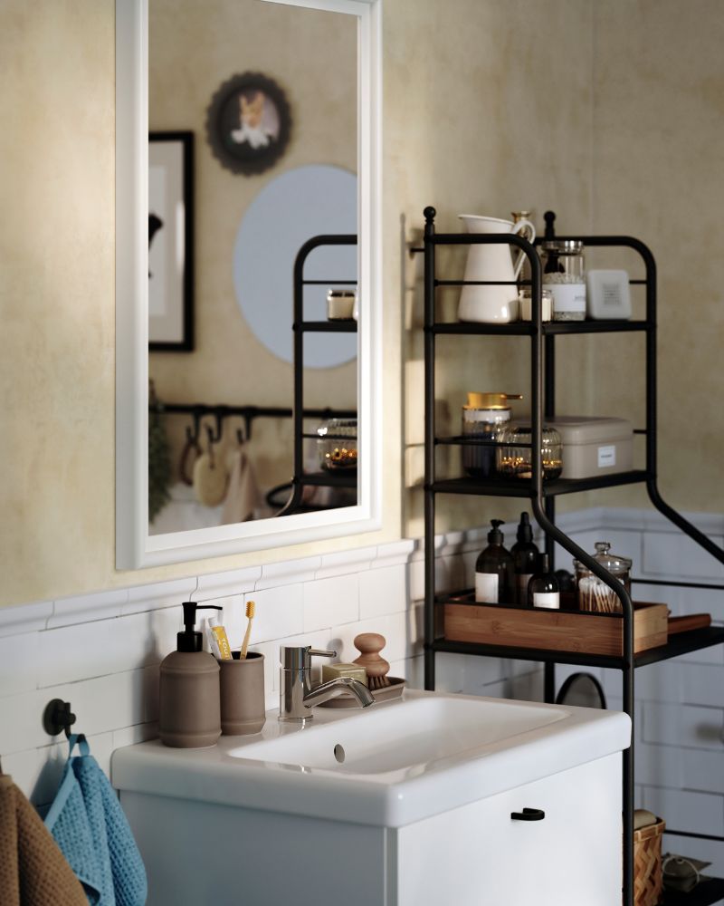 Un espejo PINGSTSYREN con marco de pino macizo pintado en blanco cuelga sobre un lavabo blanco en un baño de estilo tradicional.