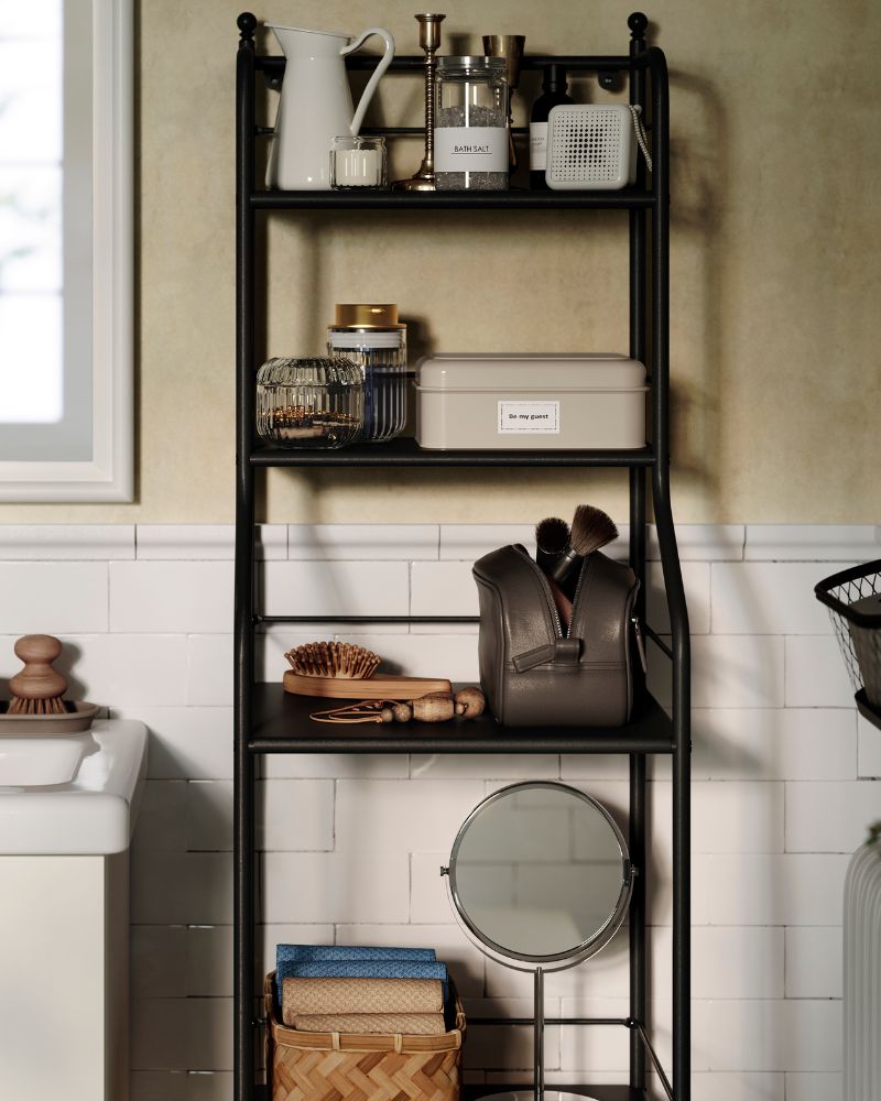 Una estantería FRÖSJÖN de metal negro sostiene artículos de aseo, elementos decorativos y toallas de mano en un baño de estilo tradicional.