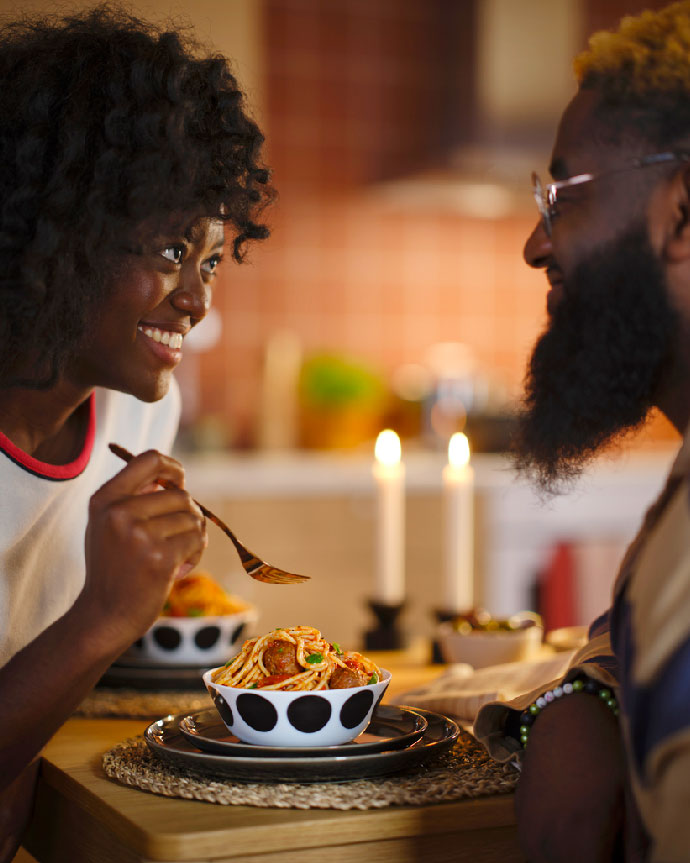Primer plano de una pareja afroamericana sonriendo mientras cenan pasta con albóndigas a la luz de las velas, creando un ambiente íntimo.