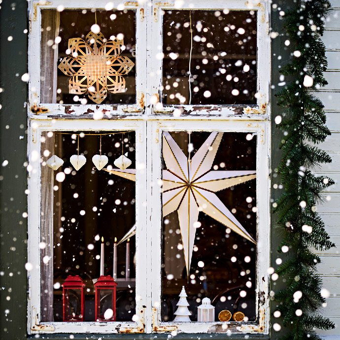 Decoración navideña de ventana rústica nevada con estrellas colgantes de papel, corazones y faroles rojos.